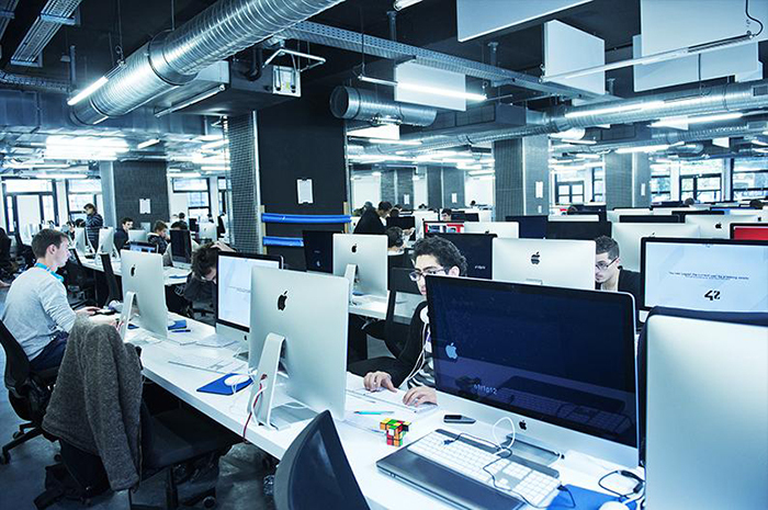 Grande salle de travail où sont aligner des dizaines d'écran d'ordinateurs sur de longue table de travail